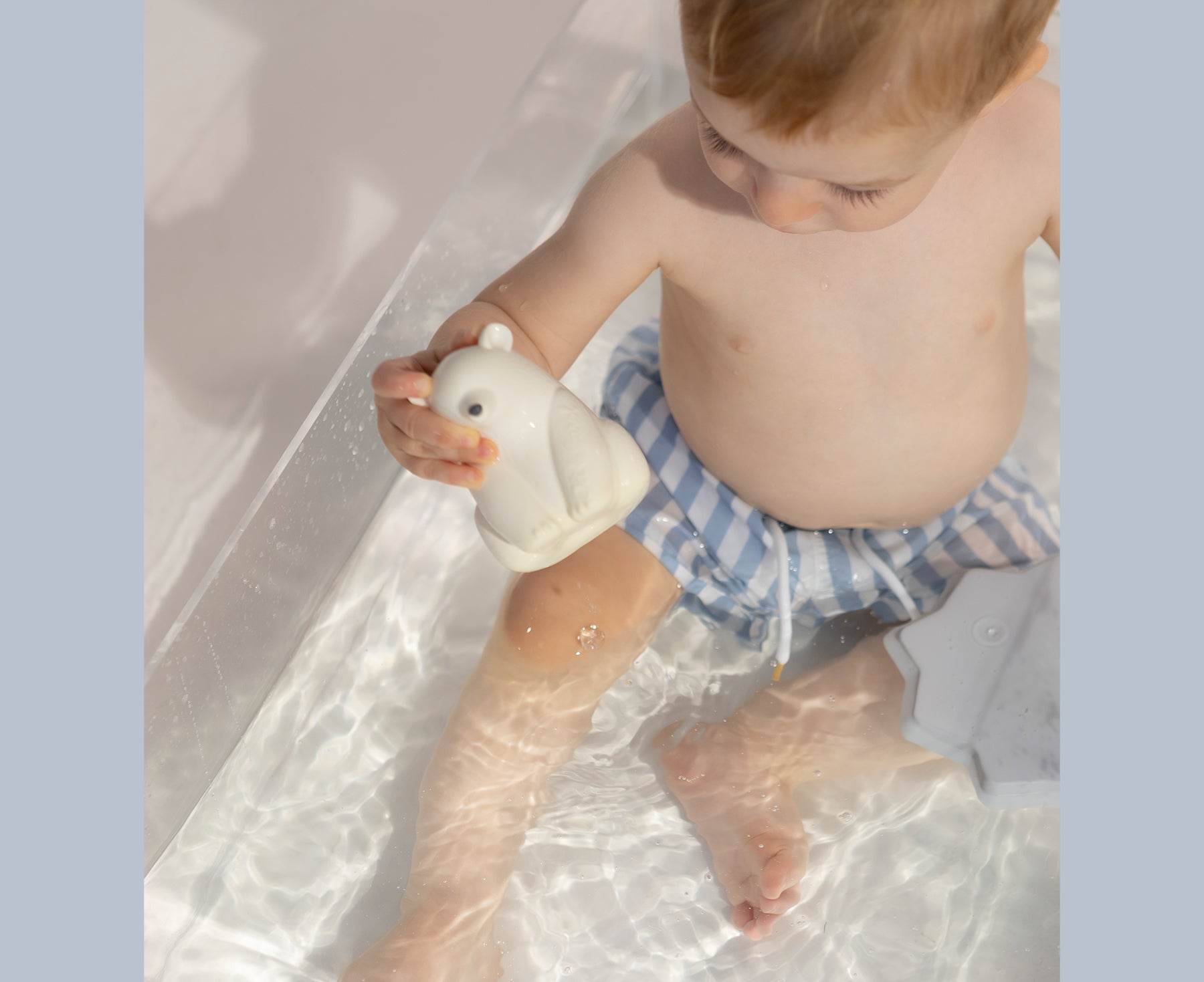 Child playing with a white polar bear chewable toy with Oli & Carol branding.